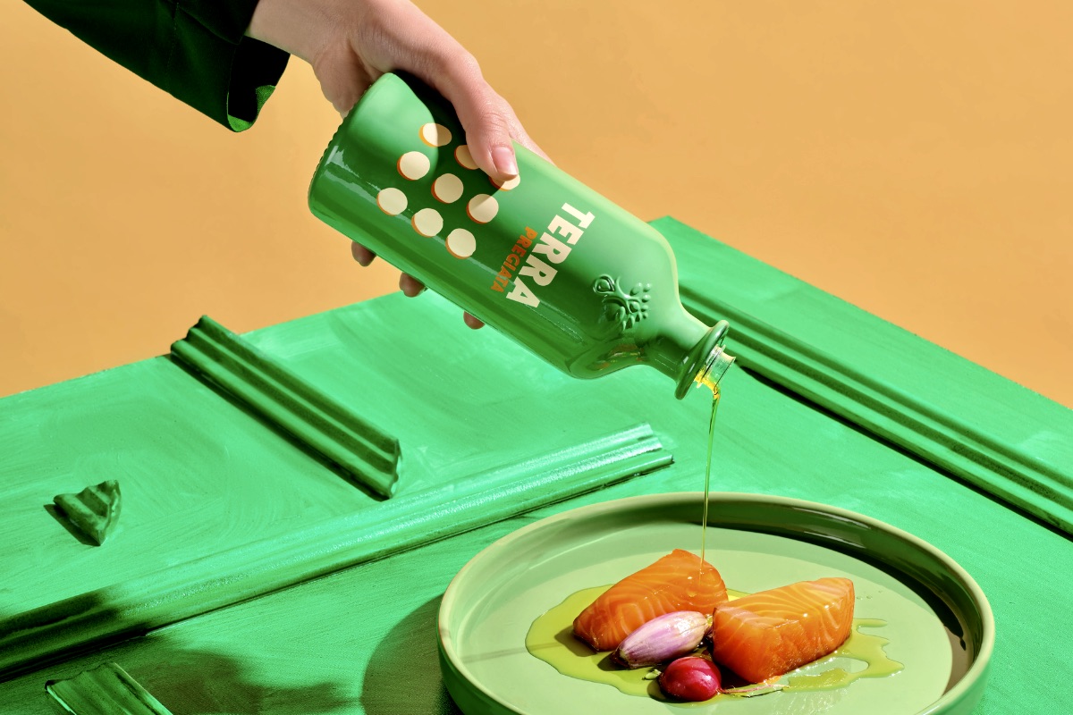 Eine Hand gießt Olivenöl aus einer grünen Tales-Flasche auf Lachs auf einem grünen Teller